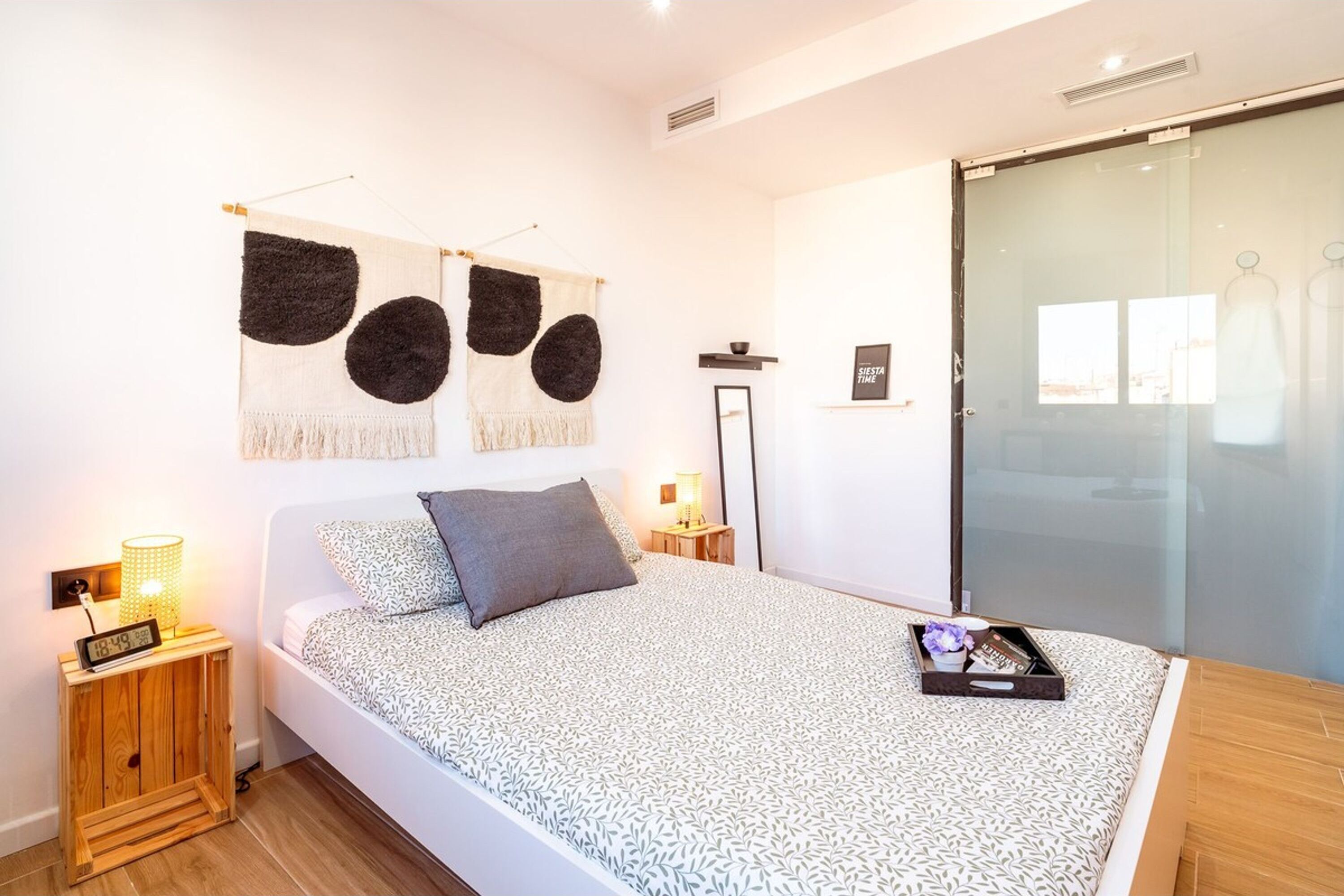 Un dormitorio moderno con cama, mesita de noche, un reloj en la pared, un cuadro enmarcado y una puerta corrediza de cristal.