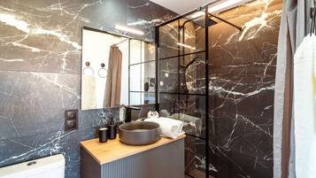 A modern bathroom with a marble backsplash, a wooden vanity, a large mirror, and a glass shower enclosure.