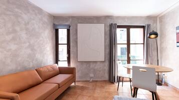 A modern living room with a leather sofa, a dining table with chairs, a floor lamp, and a large abstract painting on the wall.