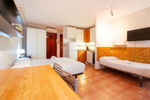 Cozy retreat with a kitchenette, featuring a single bed, a second bed, a dining table, and a flat-screen TV.
