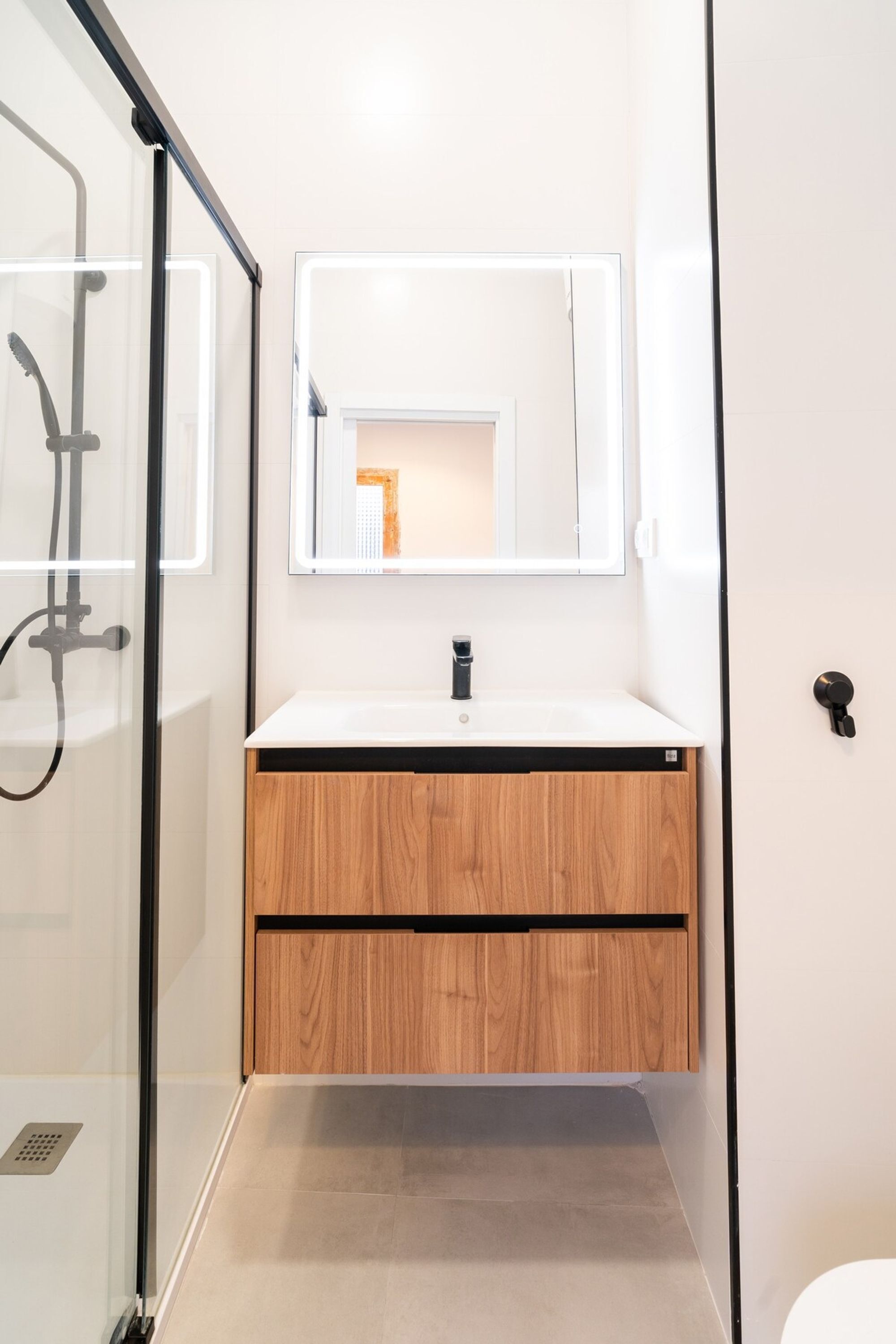 Une salle de bain avec une douche à parois de verre, un lavabo blanc et un meuble-lavabo en bois.
