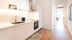 A modern kitchen with white cabinetry, a stainless steel sink, a built-in oven, and a patterned rug. - Unik Vacation C s del Bou (Tarragona)