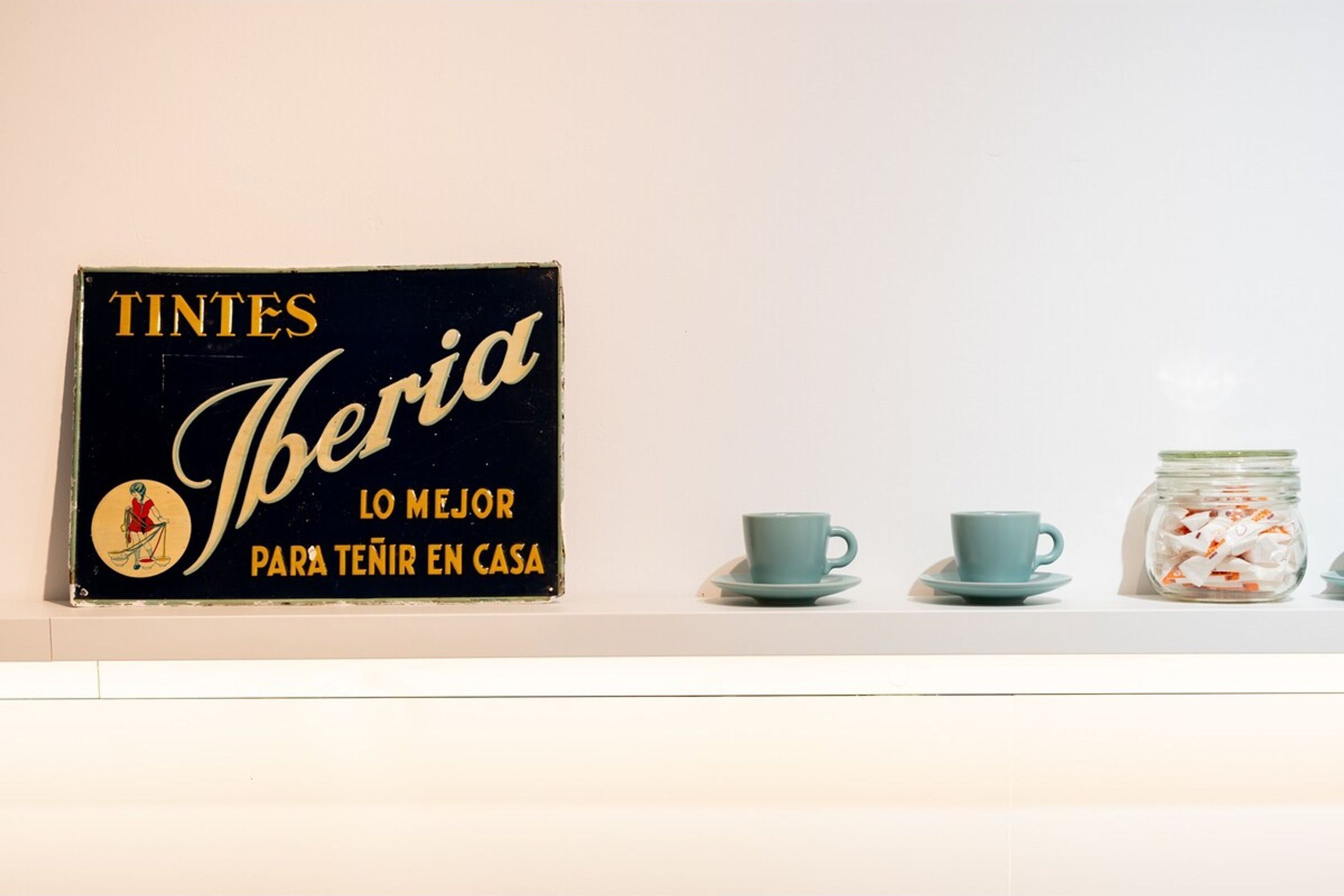 A black sign with gold lettering and a small illustration, two matching blue cups on a saucer, and a jar of cookies.