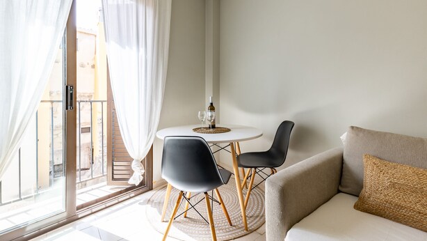 Ein modernes Wohnzimmer mit rundem Tisch, zwei Stühlen, einer Couch und Blick durch eine Glastür.