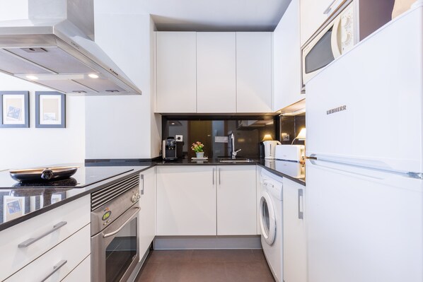 A compact kitchen with a built-in oven, microwave, and washing machine.