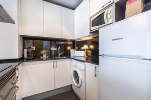 A modern kitchen with white cabinets, a built-in washing machine, a microwave, and a refrigerator.