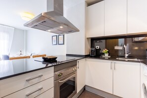 A modern kitchen with a stainless steel range hood, white cabinetry, a black countertop, and a built-in oven.