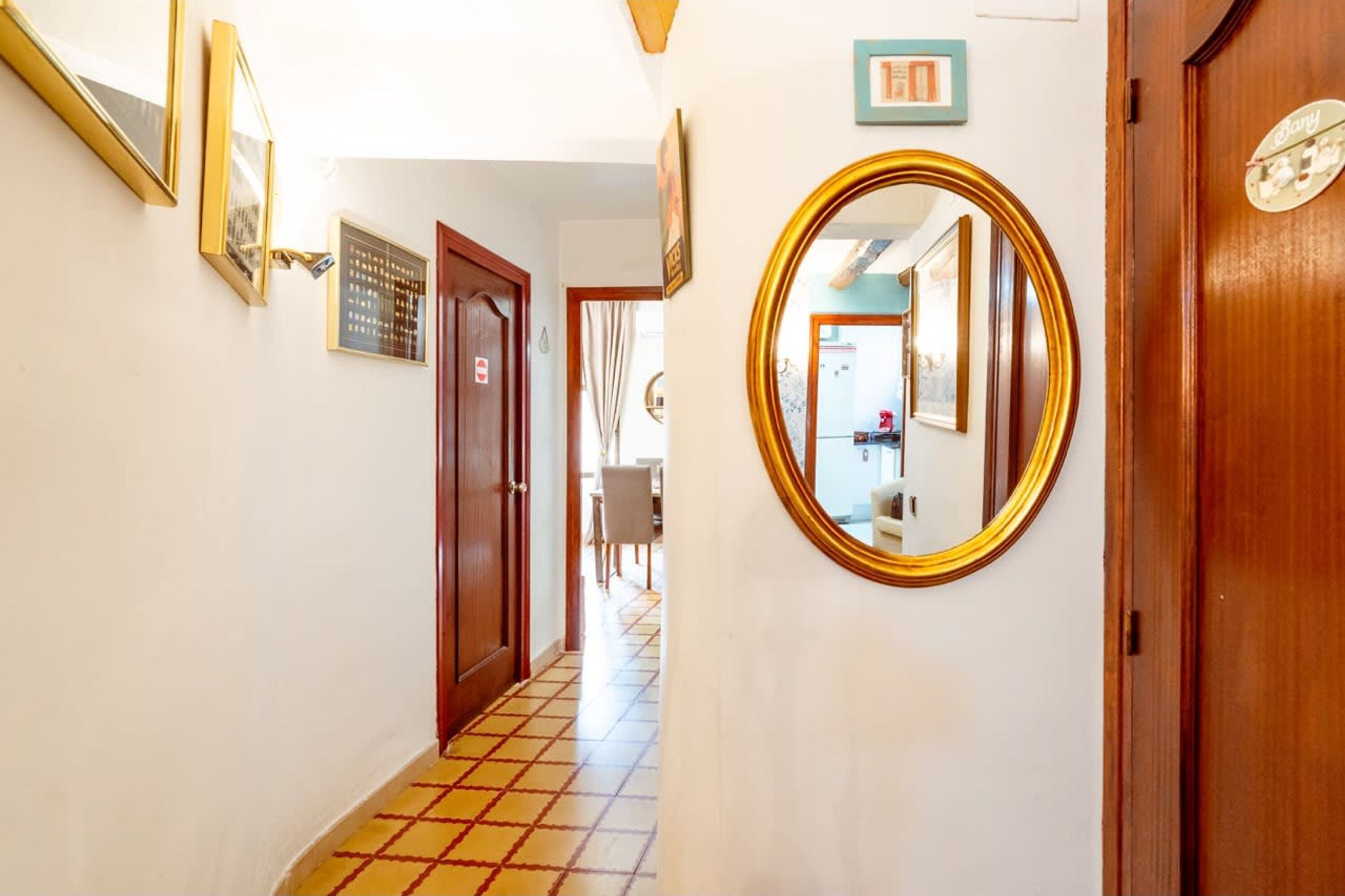Um corredor com chão de azulejos, porta de madeira e espelho na parede.