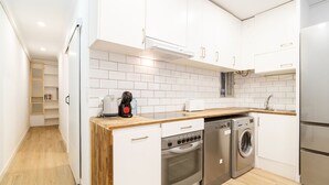 Uma cozinha moderna com armários brancos, bancada de madeira, forno embutido, lava-louças e máquina de lavar roupa.