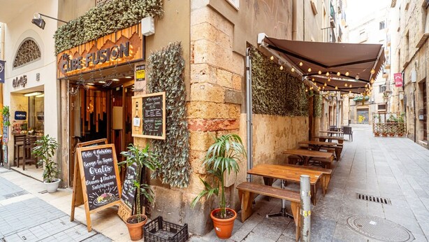 A cozy outdoor café with wooden tables and benches, surrounded by potted plants and a chalkboard menu. - Unik Vacation Dames i Vells (Tarragona)