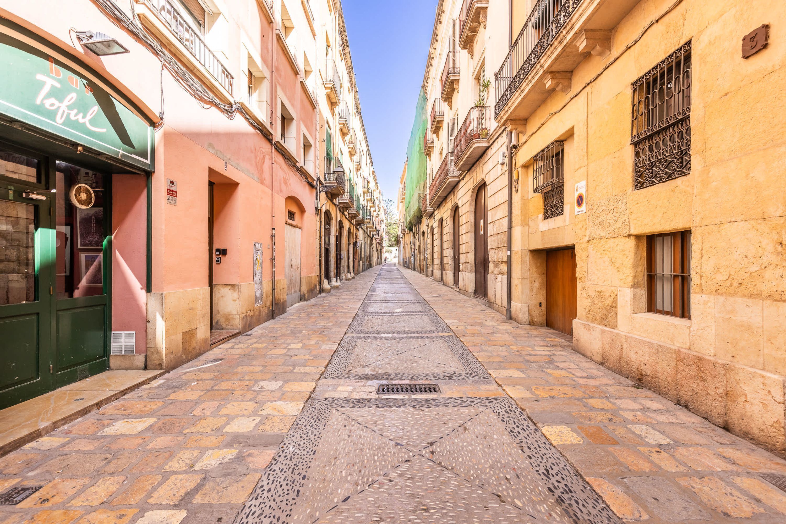 A narrow street with buildings on either side, a clear sky, and a sign for a restaurant named 'Tofu'.