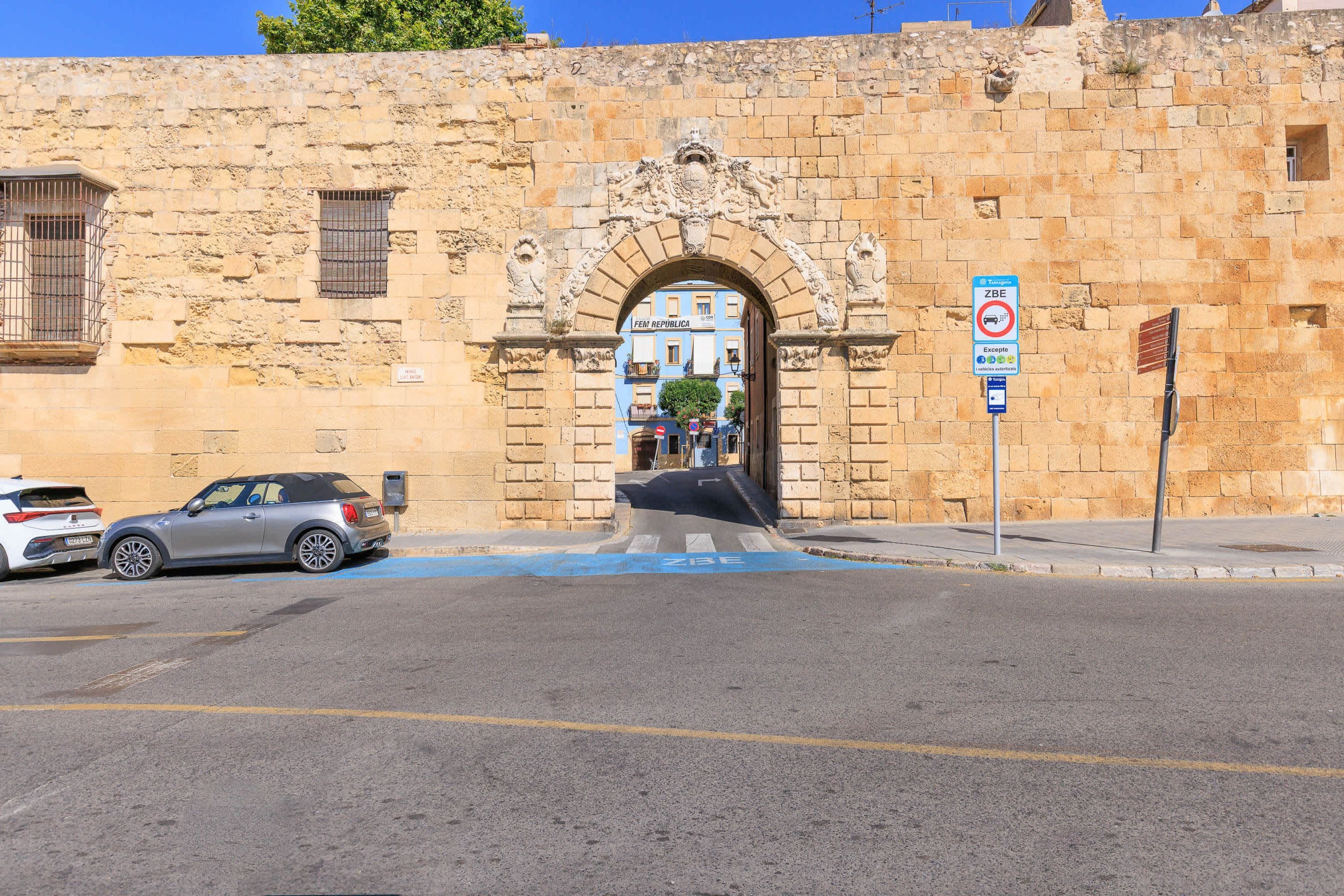 Un edificio storico in pietra con un elaborato portale ad arco, un'area di parcheggio con un'auto e un segnale di divieto di sosta.