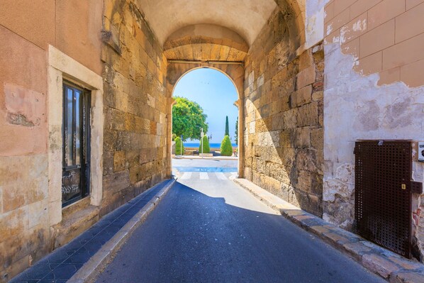 A narrow street with stone walls and an archway leading to a view of the sea. - Unik Vacation En Granada (Tarragona)