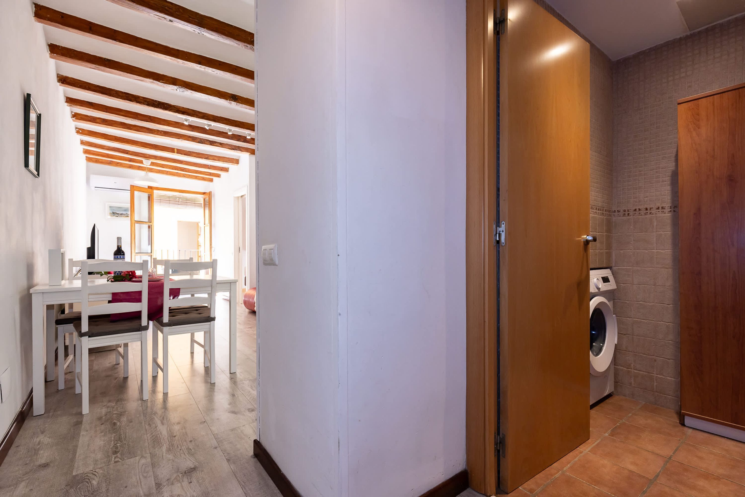 A hallway with a wooden ceiling, a white wall, a wooden door, and a washing machine in the corner.