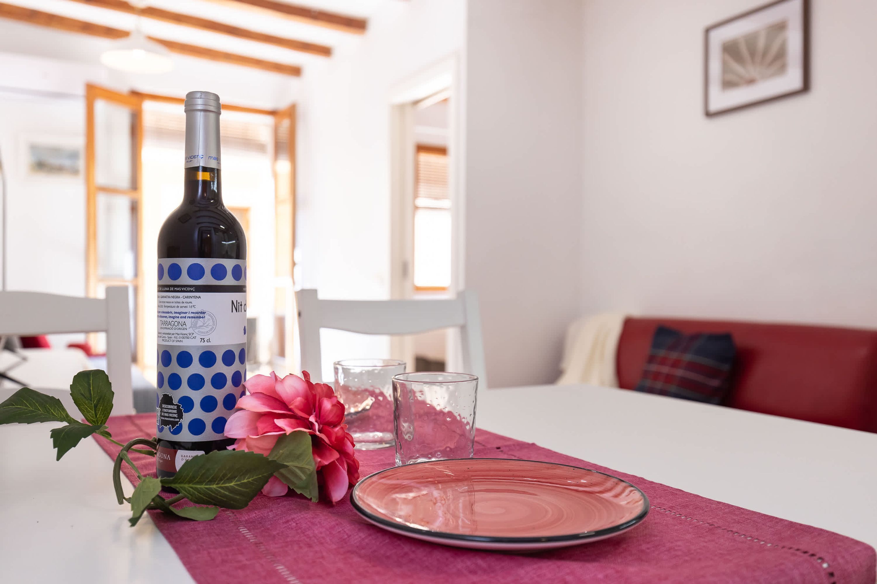 A dining table with a bottle, glasses, a plate, and a flower.