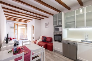 Une cuisine compacte équipée d’un lave-vaisselle, d’un four à micro-ondes et d’un four traditionnel. On y trouve également un coin repas avec une table et des chaises, ainsi qu’un canapé rouge.
