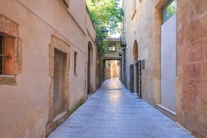 Une ruelle étroite aux murs de pierre et au sol carrelé, qui mène à l’entrée d’un immeuble.