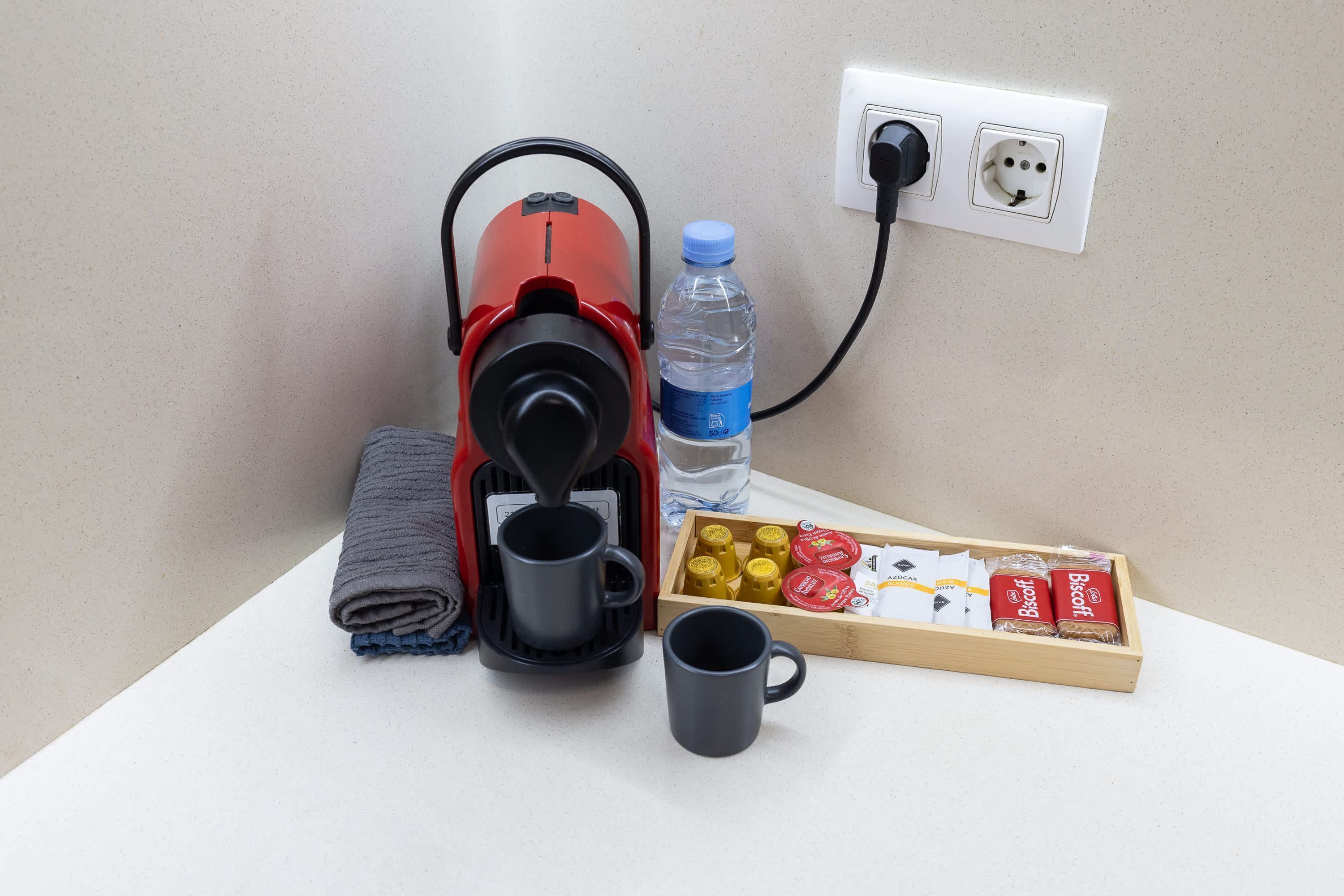 Una cafetera, una botella de agua, una taza y una caja de bizcochitos sobre una superficie blanca.