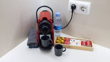 Una cafetera, una botella de agua, una taza y una caja de bizcochitos sobre una superficie blanca.