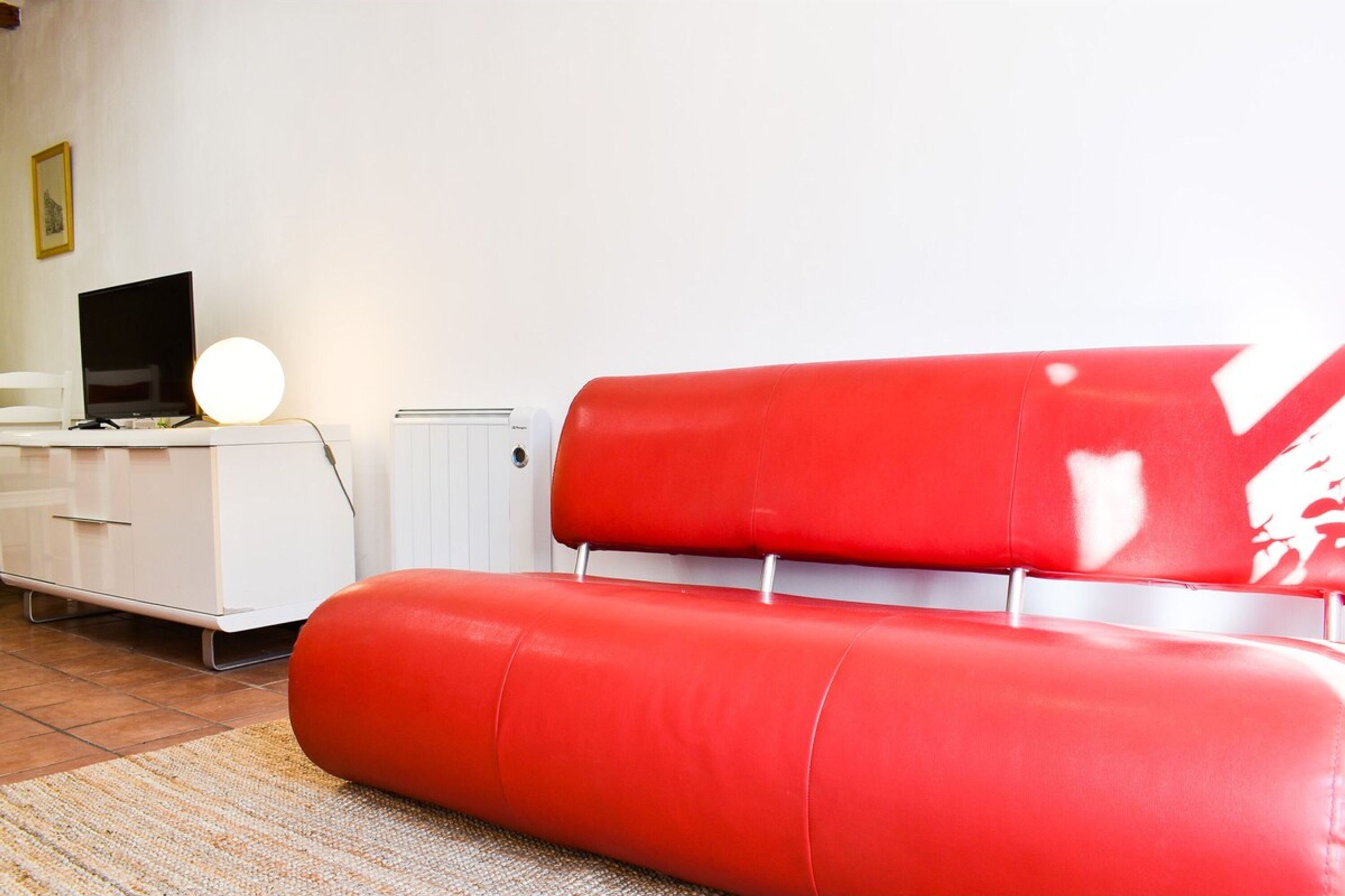 A modern living room with a red sofa, a white dresser, and a television.