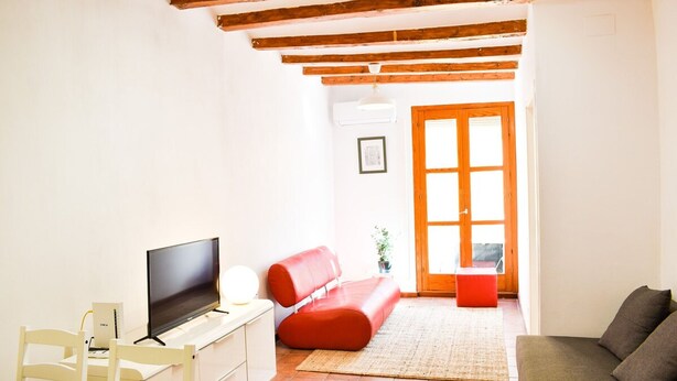Une petite pièce lumineuse, équipée d’un téléviseur, d’un canapé rouge, d’une table blanche et d’un plafond en bois.