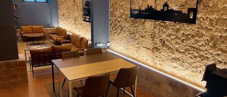 Un espace lounge moderne avec un mur en pierre, une œuvre d’art représentant un paysage urbain, des sièges en cuir et une table en bois.