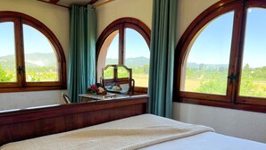 A bedroom with a large bed, a wooden dresser, a mirror, and a view of the countryside through arched windows. - Unik Vacation La Noguera Rural Valls (Valls)