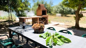 An outdoor dining area with a brick oven, green chairs, and a table with a potted plant and a bottle of wine. - Unik Vacation La Noguera Rural Valls (Valls)