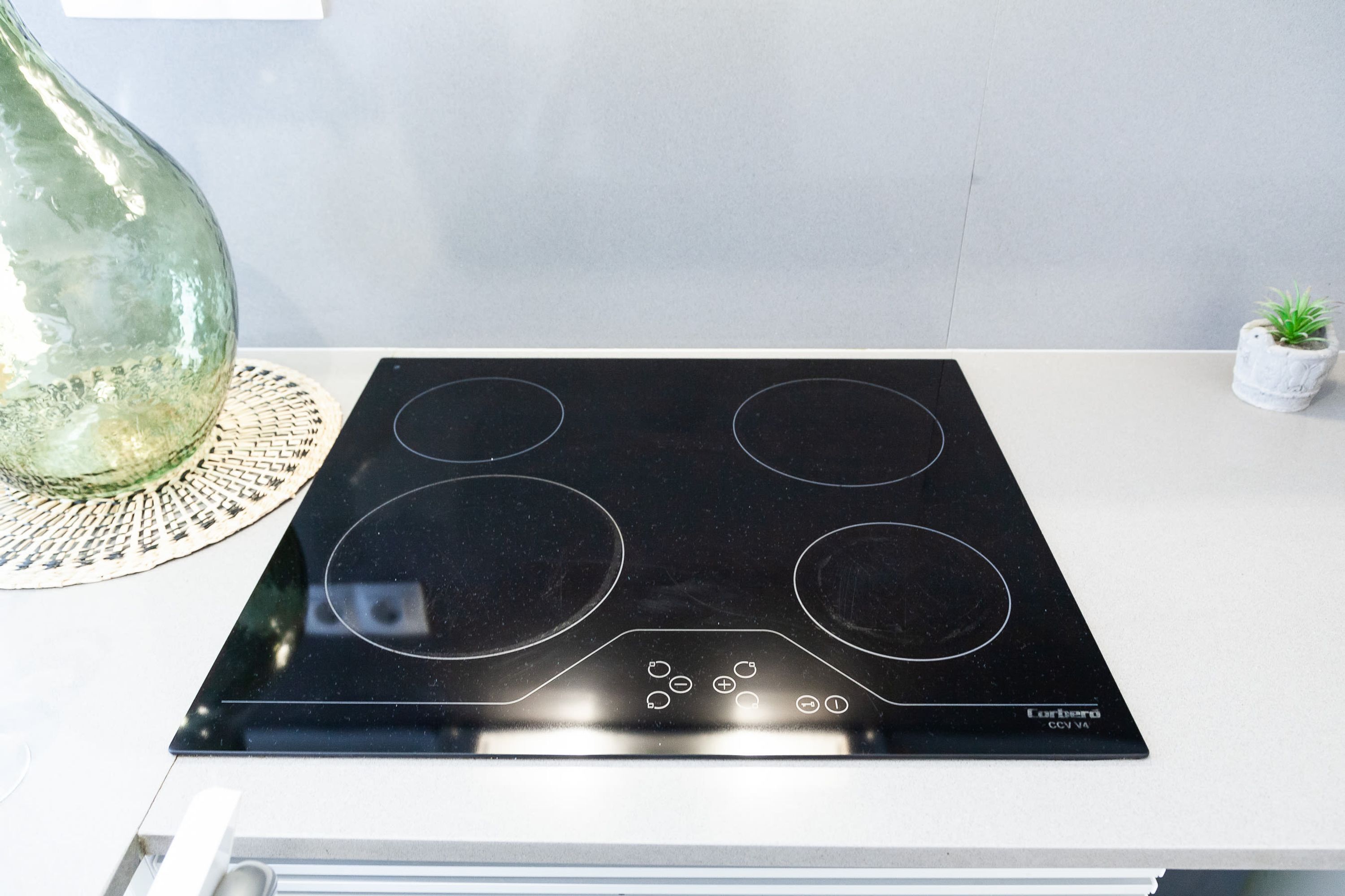 Una cocina con tope de inducción negro, un florero verde grande y una planta pequeña en maceta.