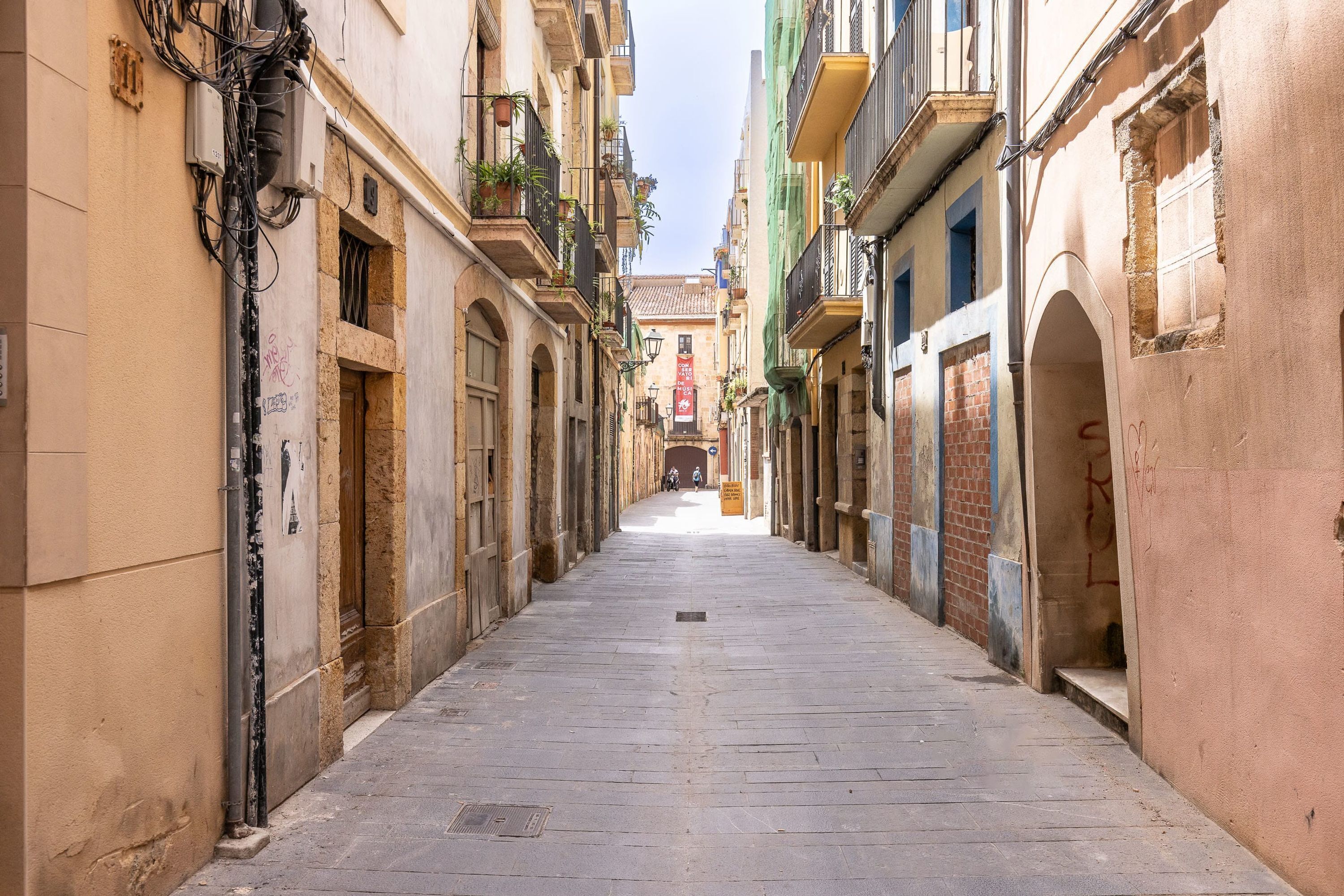 A narrow street flanked by buildings with balconies and arched doorways.