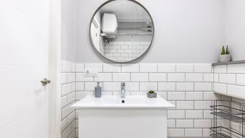 Un baño moderno con lavamanos blanco, espejo redondo y paredes revestidas con azulejos.