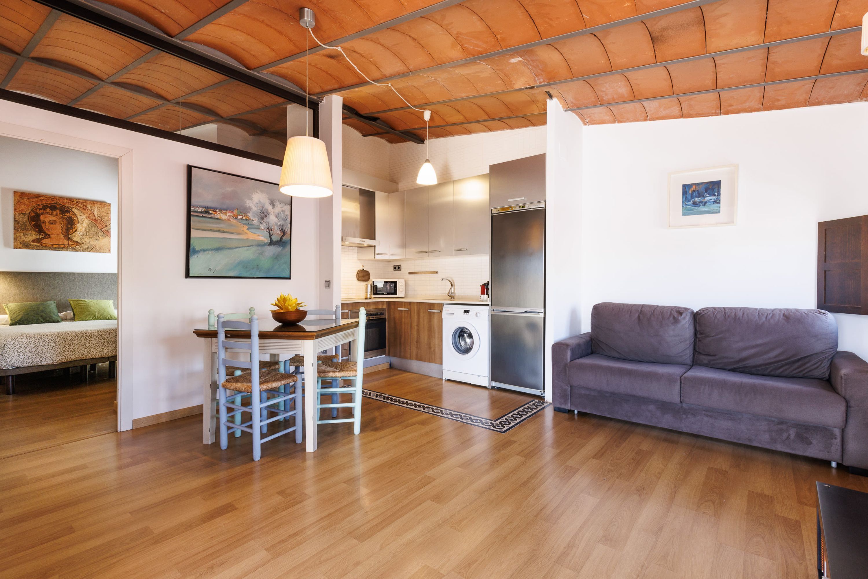 Una cocina moderna con armarios de madera, lavadora integrada y un sofá gris.