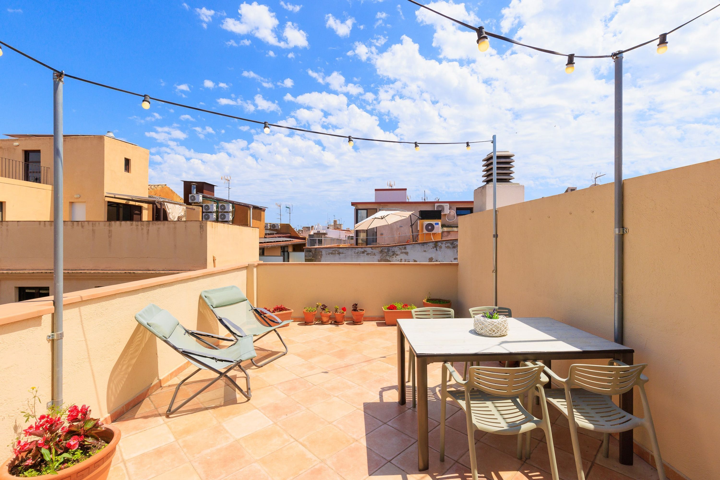 A rooftop terrace with a table and chairs, potted plants, and string lights.