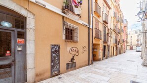 A narrow street with buildings on both sides, featuring a door with a sign, a window with barred shutters, and a wall with graffiti and a cat drawing. - Unik Vacation Ferrers (Tarragona)