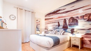 A bedroom with a bed, nightstands, a clock, and a mural of a coastal scene. - Unik Vacation Ferrers (Tarragona)