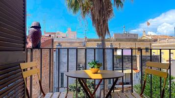 A balcony with a table and two chairs, overlooking a cityscape with buildings and a palm tree.