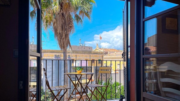 A balcony with a table and chairs, a potted plant, and a view of buildings and palm trees. - Unik Vacation Ferrers (Tarragona)