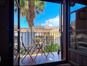 A balcony with a table and chairs, a potted plant, and a view of buildings and palm trees. - Unik Vacation Ferrers (Tarragona)