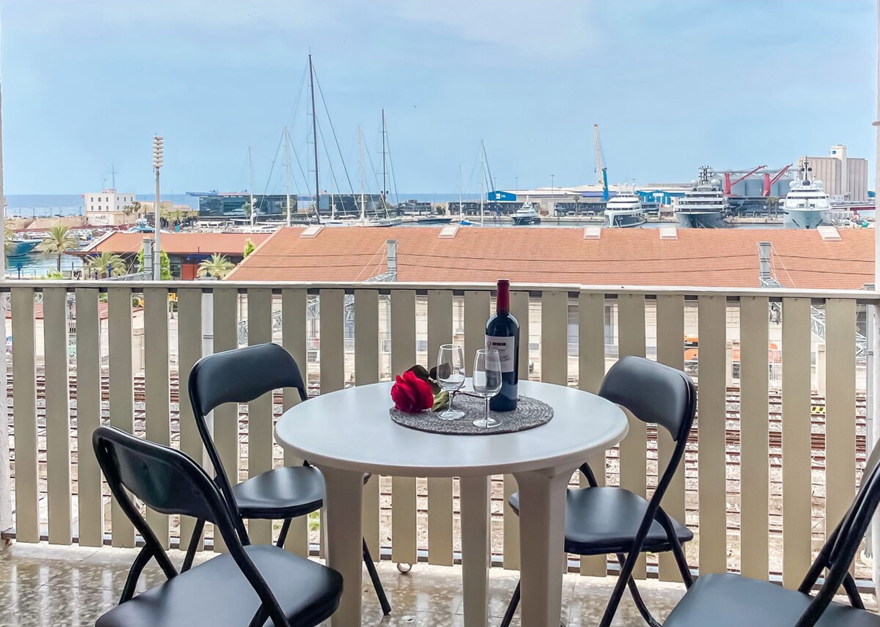 A balcony with a round table, two chairs, a bottle of wine, and a red rose.