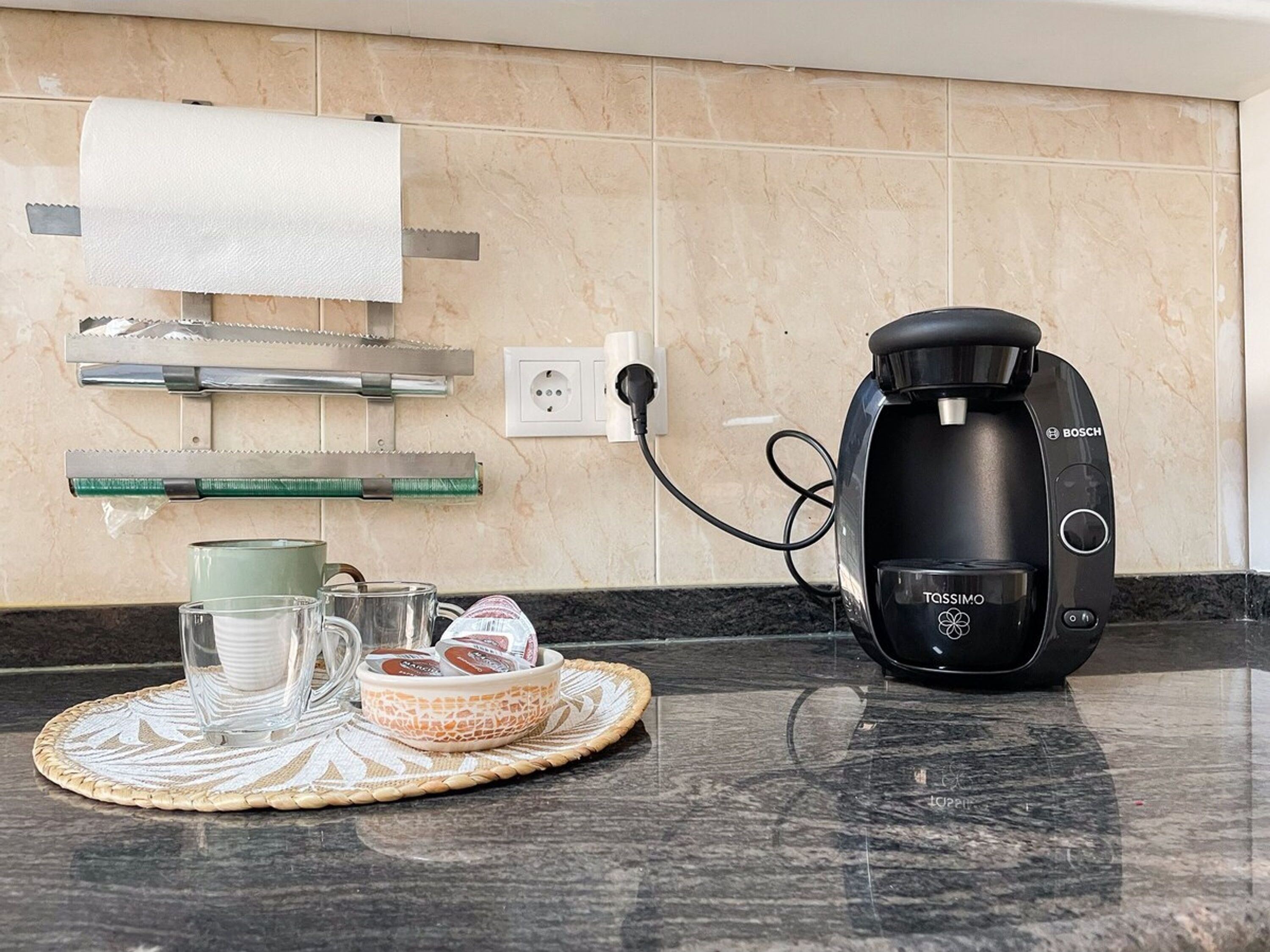 A kitchen with a Bosch coffee maker, a glass of water, a cup, and a basket of pastries on a marble countertop.