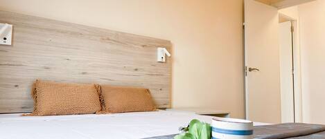 A neatly made bed with a headboard, a blue-striped mug on a coaster, and a door to the right.