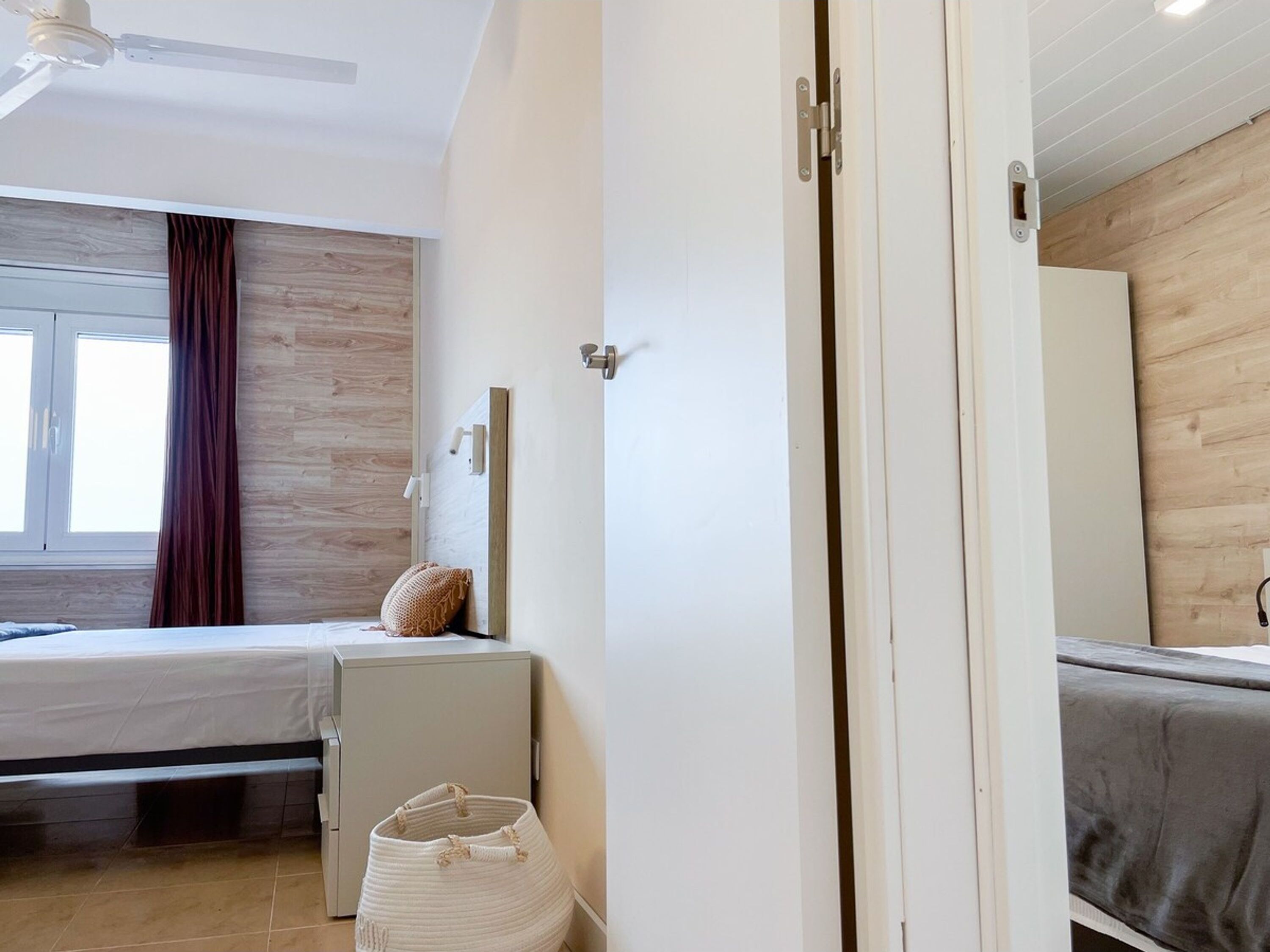 Un dormitorio moderno con cama, mesita de noche, espejo montado en la pared y ventilador de techo.
