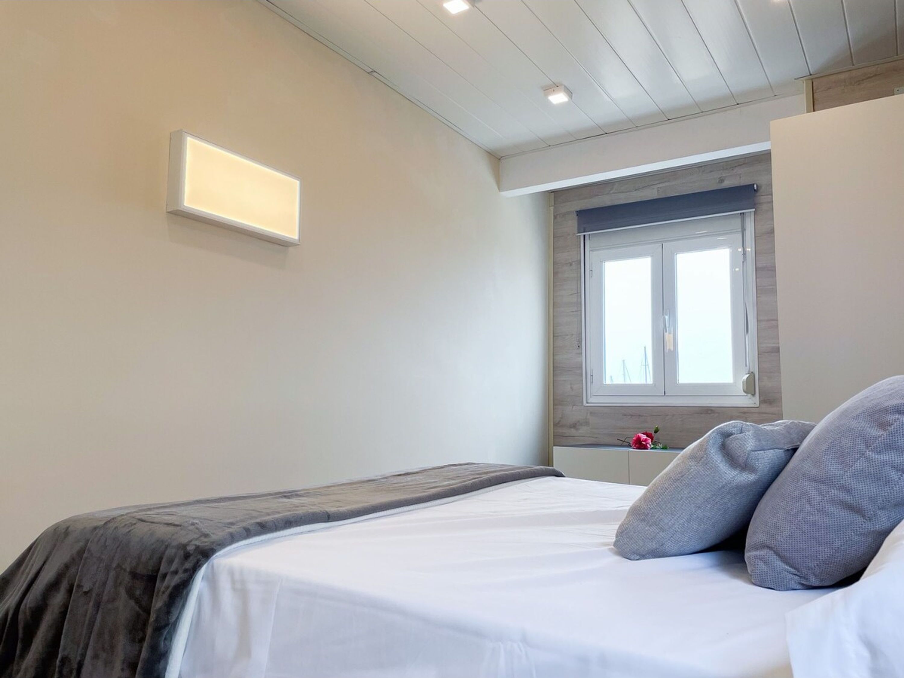 Un dormitorio con cama, ventana y lámpara en la pared.