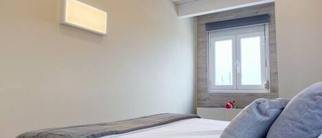 Un dormitorio con cama, ventana y lámpara en la pared.