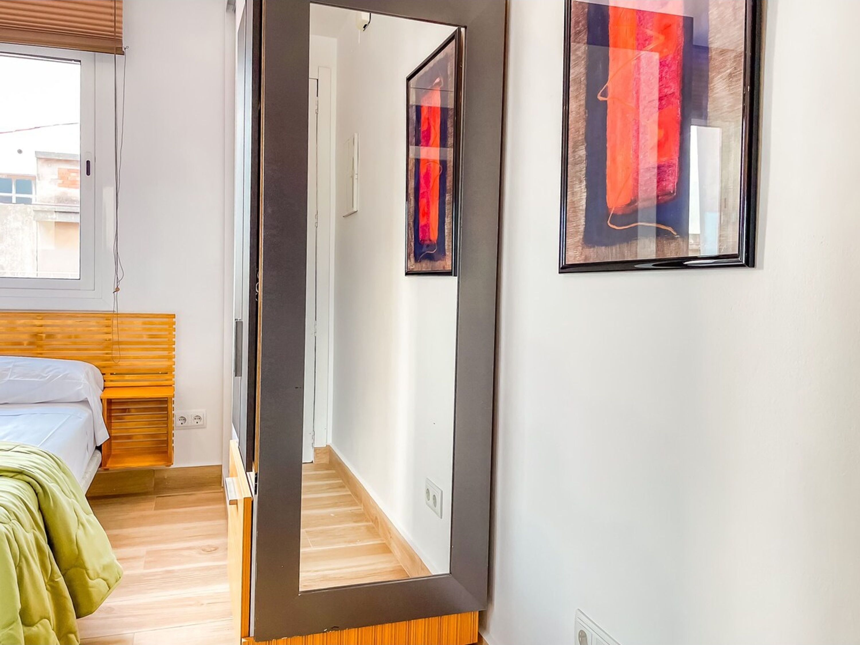A bedroom with a bed, a mirror, and a framed abstract painting on the wall.