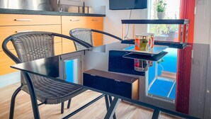 A modern kitchen with a glass dining table, wicker chairs, and a TV mounted above the counter. - Unik Vacation Attic in Tarragona (Tarragona)