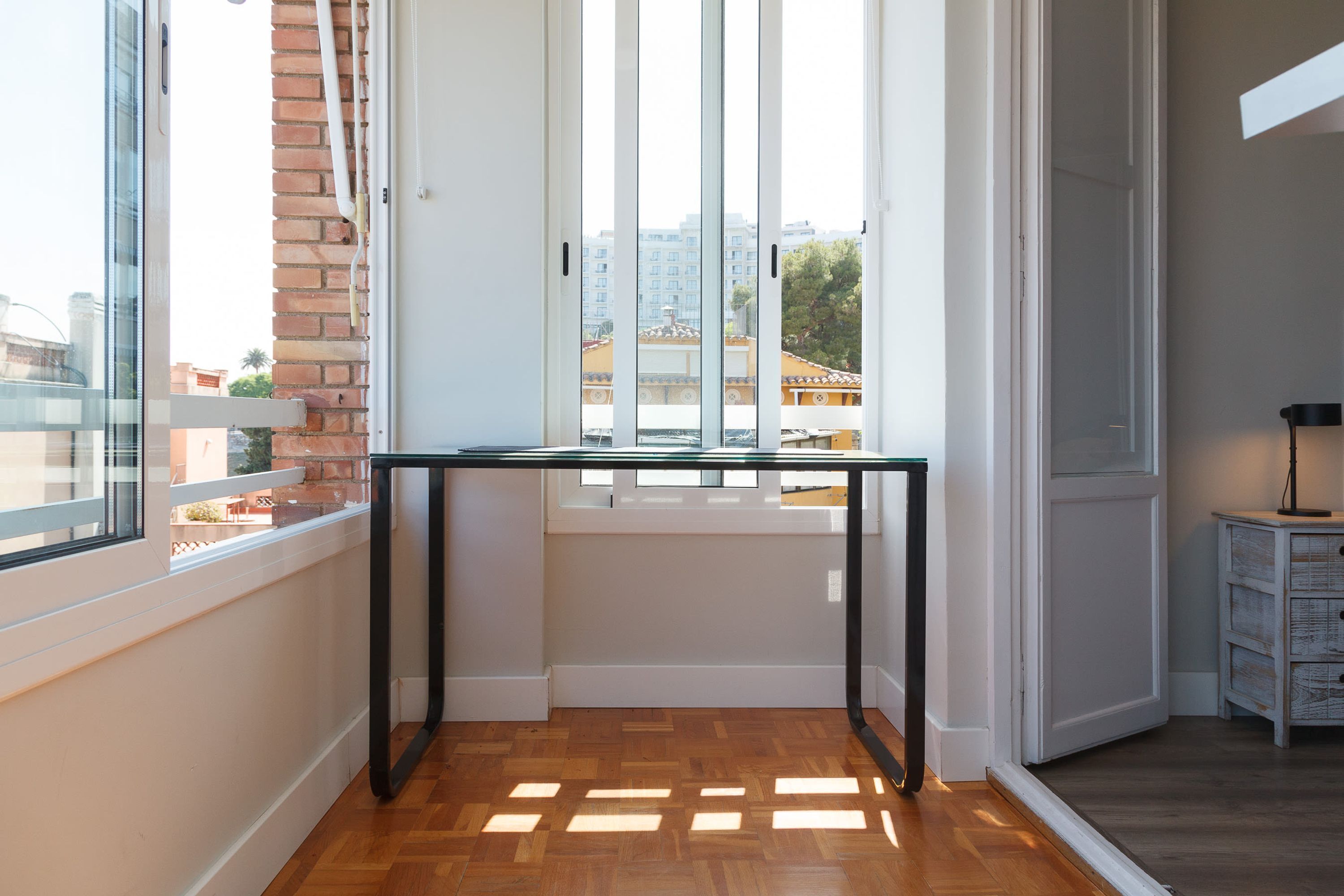 A room with a wooden floor, a glass table, a brick wall, and a view of buildings outside.