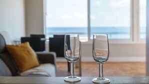 Two empty wine glasses on a wooden table in a room with a view of the ocean through large windows. - Unik Vacation Via Augusta (Tarragona)