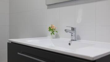 Un baño con un lavamanos blanco, un espejo y una pequeña planta en maceta.
