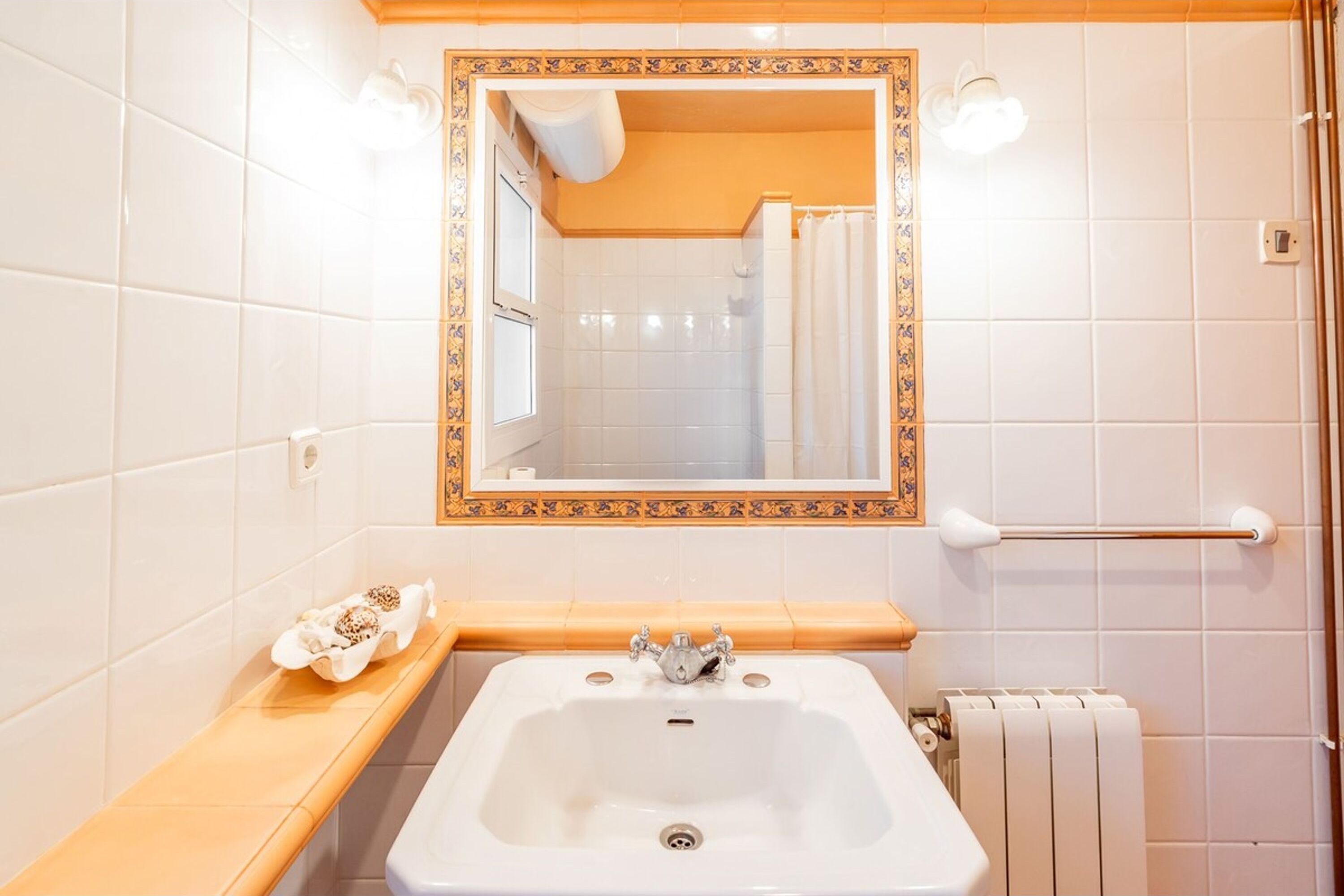A bathroom with a white sink, a mirror with a decorative frame, a towel rack, and a shelf with toiletries.